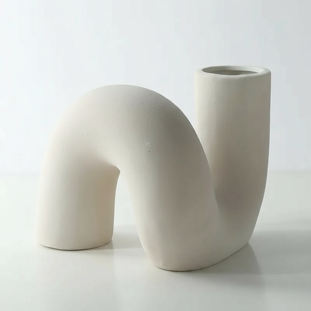 A white, minimalist, ceramic flower vase with an abstract and twisted shape.